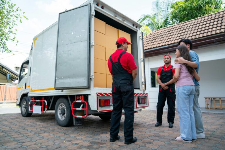 Wide shot of two delivery man opern truck door and show to couple people as customer at the house